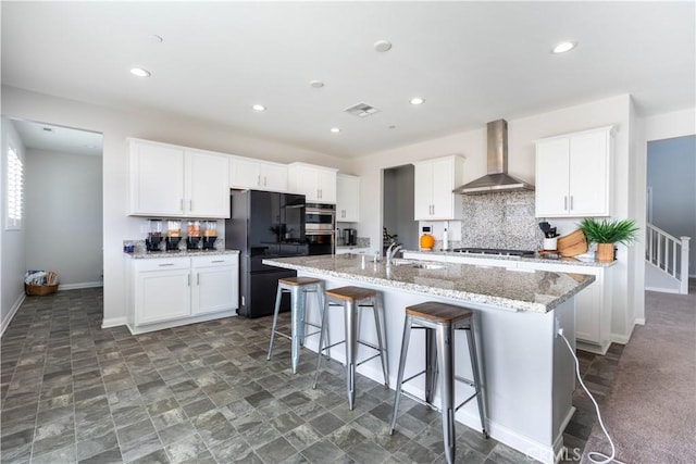 kitchen with stainless steel appliances, white cabinetry, a center island with sink, and wall chimney range hood