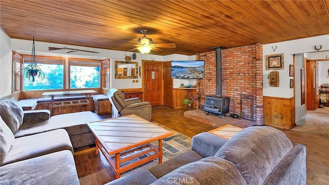 living room featuring a wood stove, ceiling fan, hardwood / wood-style floors, wooden ceiling, and wood walls