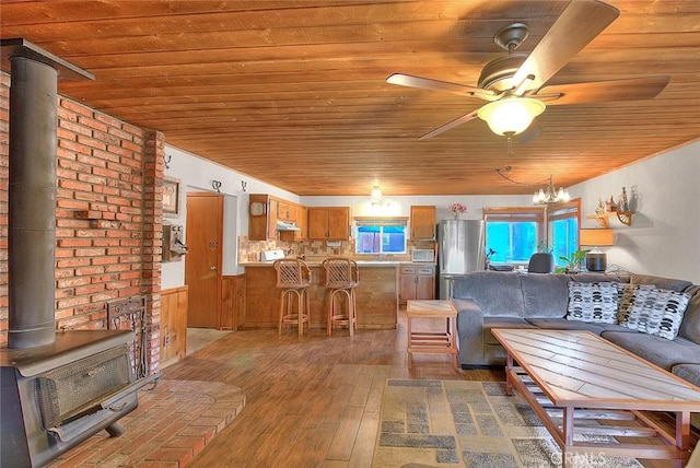 living area featuring wooden ceiling, a wood stove, wood-type flooring, and ceiling fan with notable chandelier