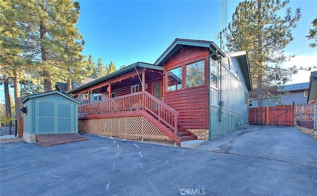back of house featuring fence, a deck, an outdoor structure, and a shed