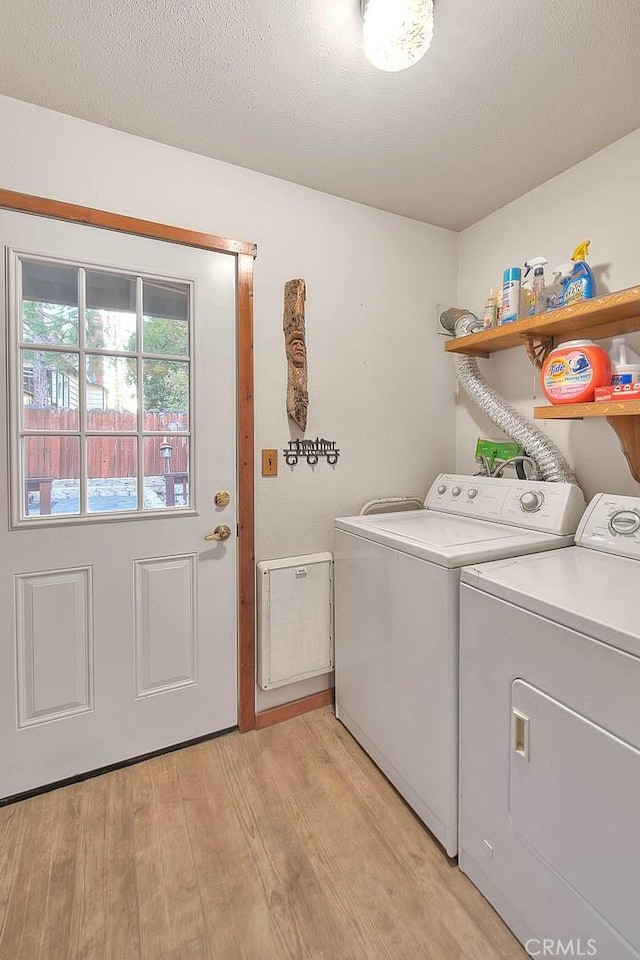 clothes washing area featuring a textured ceiling, washer and clothes dryer, and light hardwood / wood-style flooring