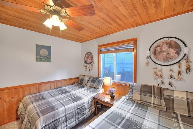 bedroom featuring wooden ceiling, ceiling fan, a wainscoted wall, and wooden walls