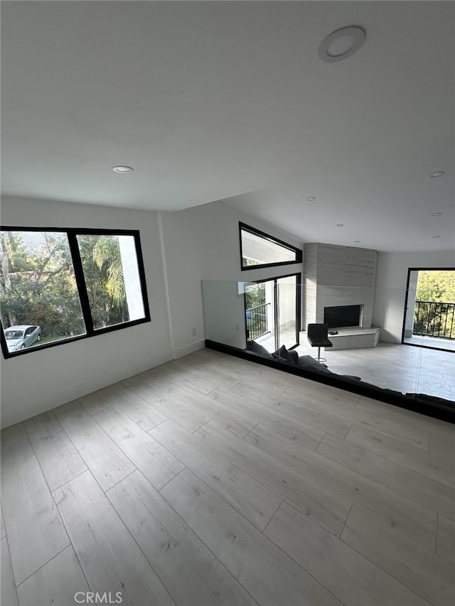 unfurnished living room with a large fireplace, a healthy amount of sunlight, and light wood-type flooring