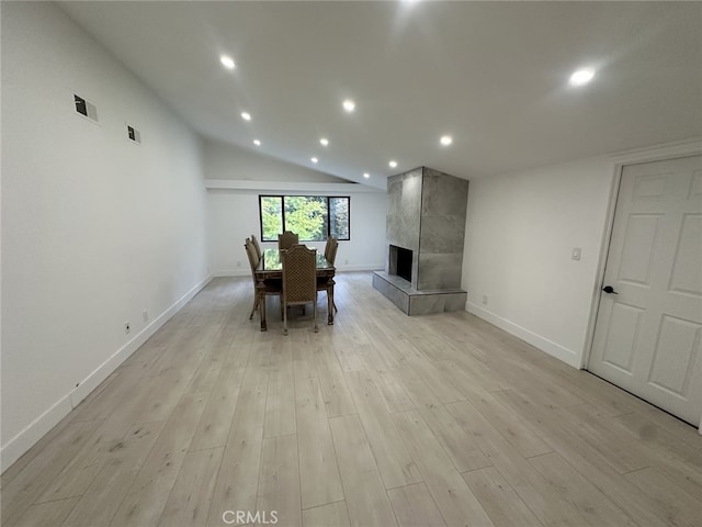 unfurnished dining area with light hardwood / wood-style floors, a tiled fireplace, and vaulted ceiling