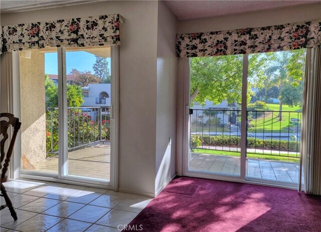 doorway to outside featuring light tile patterned floors, a textured ceiling, and a healthy amount of sunlight