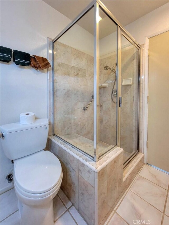 bathroom featuring tile patterned flooring, toilet, and a shower with shower door