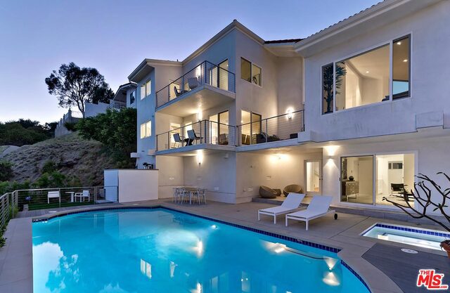 pool at dusk featuring a patio area and an in ground hot tub