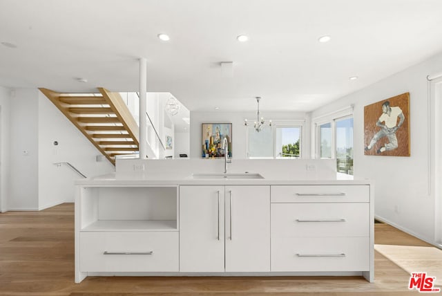 kitchen featuring sink, an inviting chandelier, light hardwood / wood-style flooring, white cabinetry, and hanging light fixtures