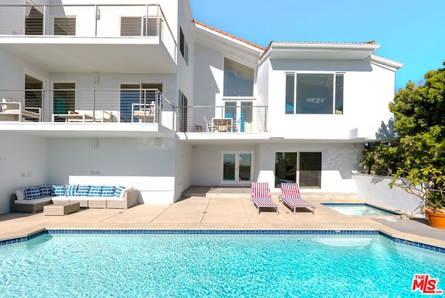 rear view of house with a swimming pool with hot tub, a balcony, and a patio