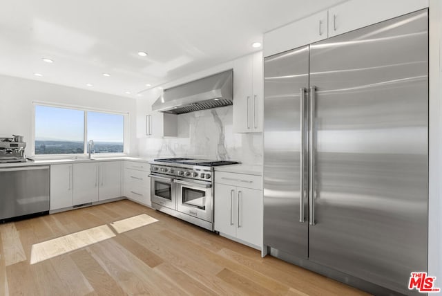 kitchen featuring decorative backsplash, wall chimney exhaust hood, light hardwood / wood-style flooring, high quality appliances, and white cabinetry