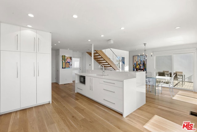 kitchen with white cabinetry, sink, light hardwood / wood-style flooring, an island with sink, and pendant lighting