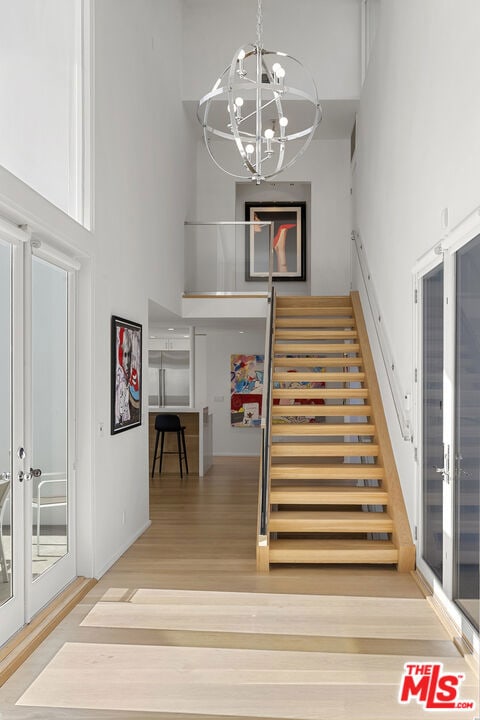 stairway featuring hardwood / wood-style flooring, a notable chandelier, a towering ceiling, and french doors