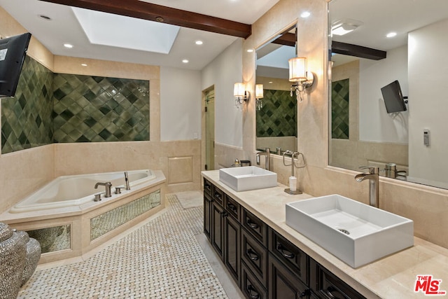 bathroom with a skylight, tile patterned floors, vanity, a bath, and tile walls