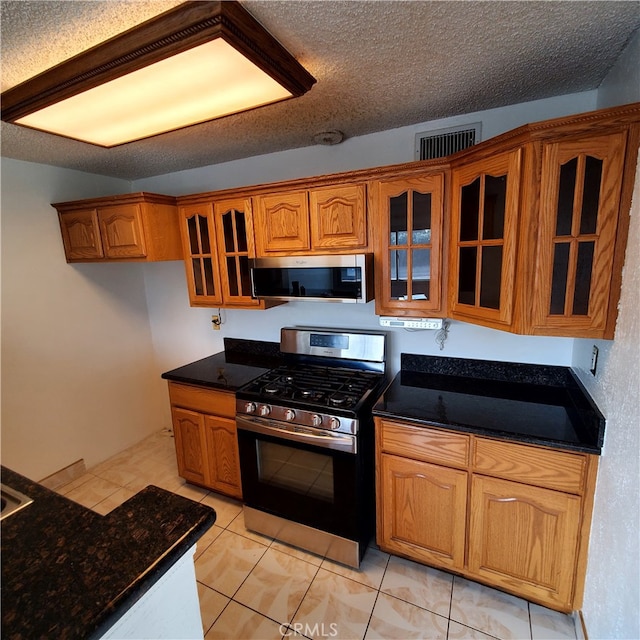 kitchen featuring dark stone countertops, light tile patterned floors, a textured ceiling, and appliances with stainless steel finishes