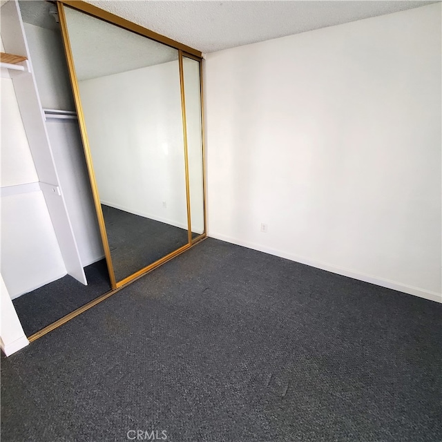 unfurnished bedroom with a closet, dark carpet, and a textured ceiling