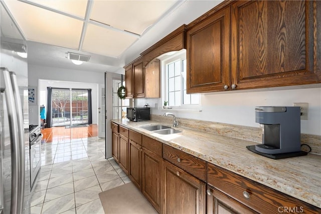 kitchen featuring stainless steel refrigerator, a healthy amount of sunlight, light stone countertops, and sink