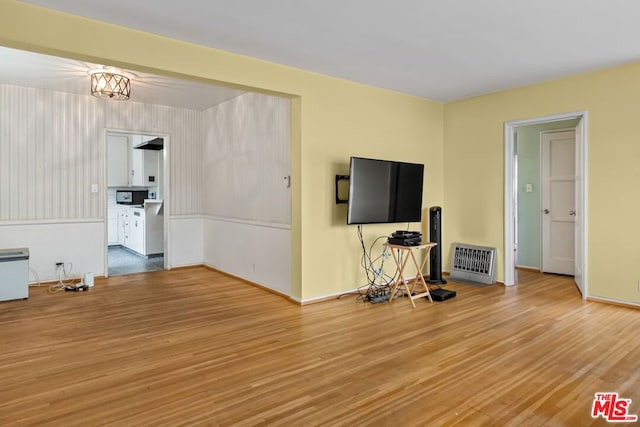 unfurnished living room featuring hardwood / wood-style floors, a notable chandelier, and heating unit