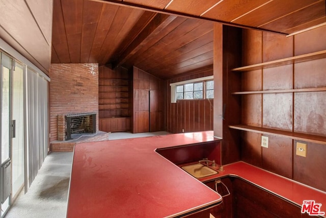 unfurnished office featuring light carpet, a brick fireplace, built in features, wooden ceiling, and vaulted ceiling with beams