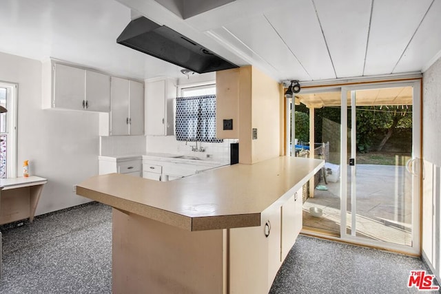 kitchen with white cabinets, backsplash, kitchen peninsula, and plenty of natural light