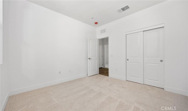 unfurnished bedroom featuring light carpet, baseboards, visible vents, and a closet