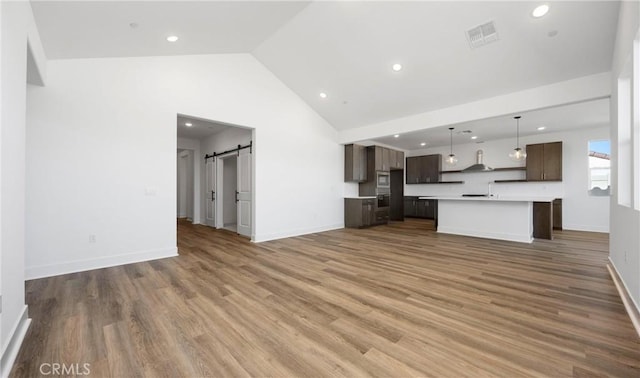 unfurnished living room featuring baseboards, a barn door, visible vents, and wood finished floors