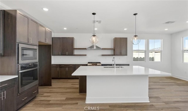 kitchen featuring stainless steel appliances, light countertops, a sink, an island with sink, and dark brown cabinets