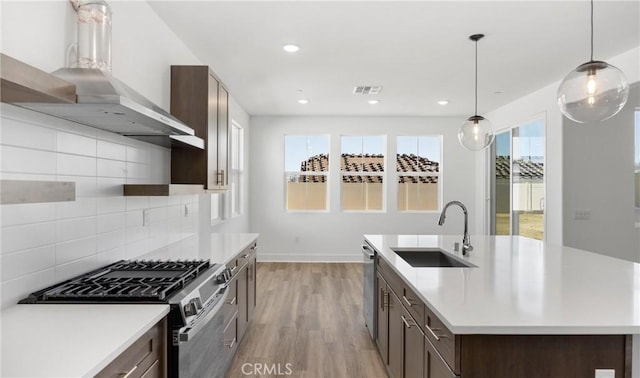 kitchen featuring wall chimney exhaust hood, hanging light fixtures, light countertops, stainless steel appliances, and a sink