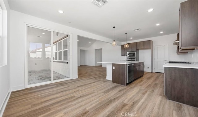 kitchen featuring pendant lighting, light countertops, visible vents, open floor plan, and a kitchen island with sink