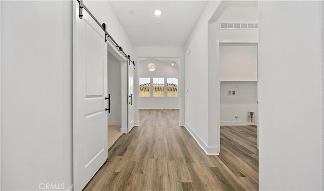 hall with a barn door, wood finished floors, visible vents, and baseboards