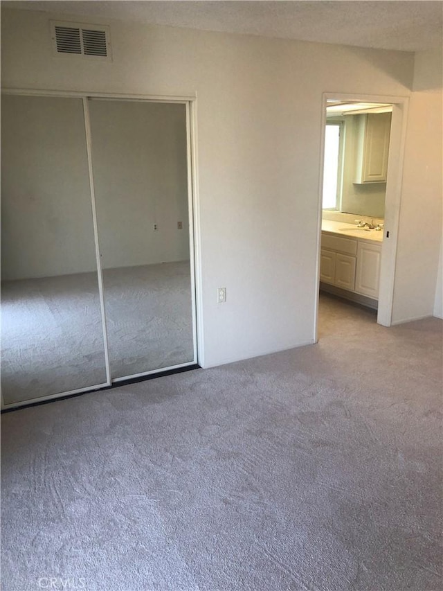 unfurnished bedroom with connected bathroom, a closet, light colored carpet, and sink