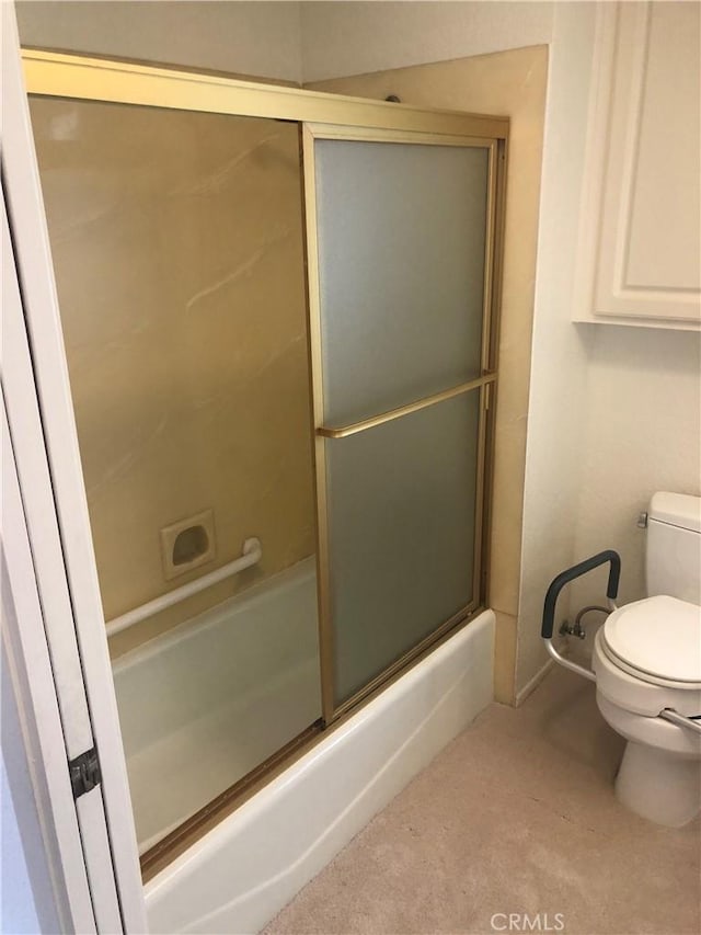 bathroom featuring toilet and bath / shower combo with glass door