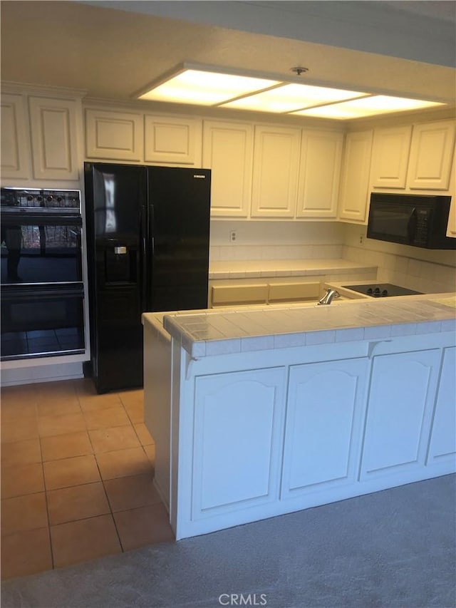 kitchen with white cabinets, light tile patterned floors, tile countertops, and black appliances