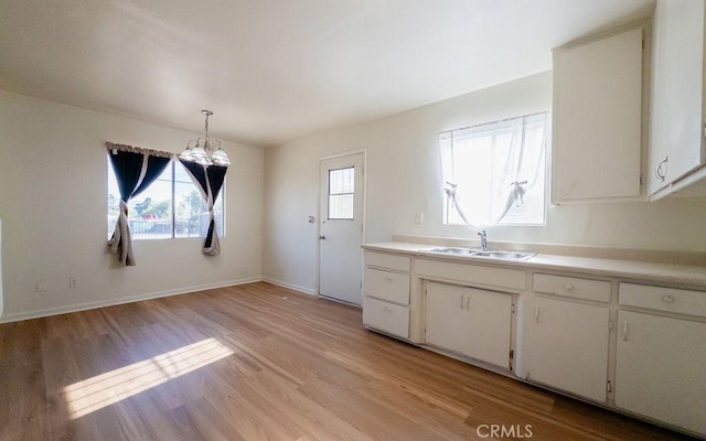 kitchen featuring decorative light fixtures, white cabinetry, an inviting chandelier, sink, and light hardwood / wood-style flooring