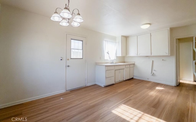 kitchen with pendant lighting, white cabinets, an inviting chandelier, sink, and light hardwood / wood-style flooring