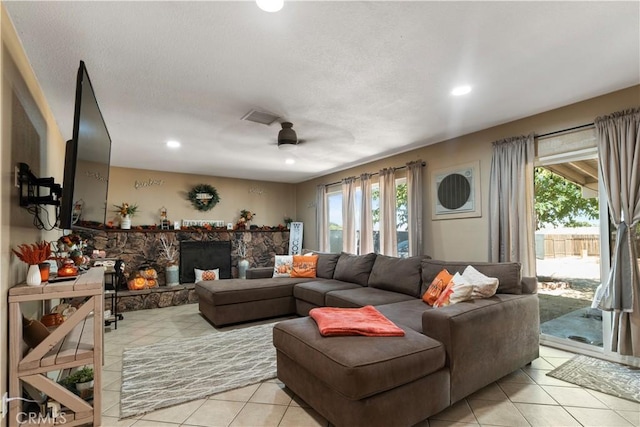 tiled living room with ceiling fan and a stone fireplace