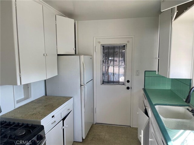 kitchen with stainless steel range with gas cooktop, white cabinets, sink, and tasteful backsplash