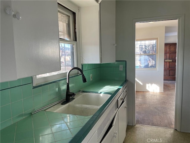 kitchen with light tile patterned floors, tile counters, white cabinets, and sink