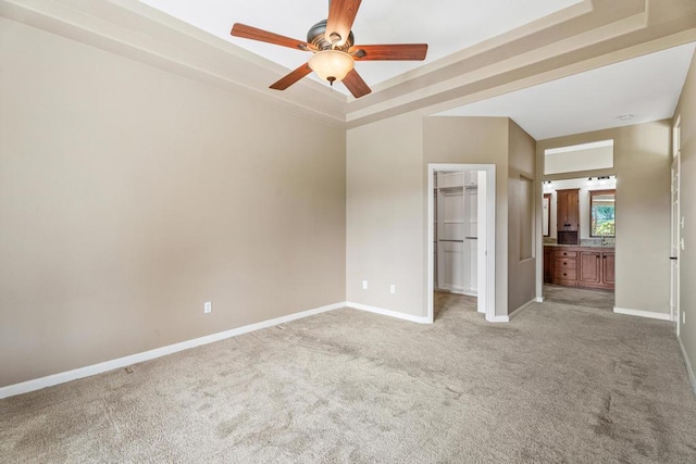 unfurnished bedroom featuring a walk in closet, a closet, a raised ceiling, and ceiling fan