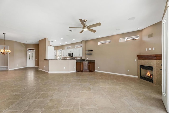 unfurnished living room featuring ceiling fan with notable chandelier, light tile patterned floors, and a tile fireplace