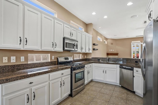 kitchen featuring stainless steel appliances, sink, light tile patterned floors, dark stone countertops, and white cabinetry