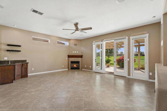 unfurnished living room with a tile fireplace, ceiling fan, and light tile patterned floors