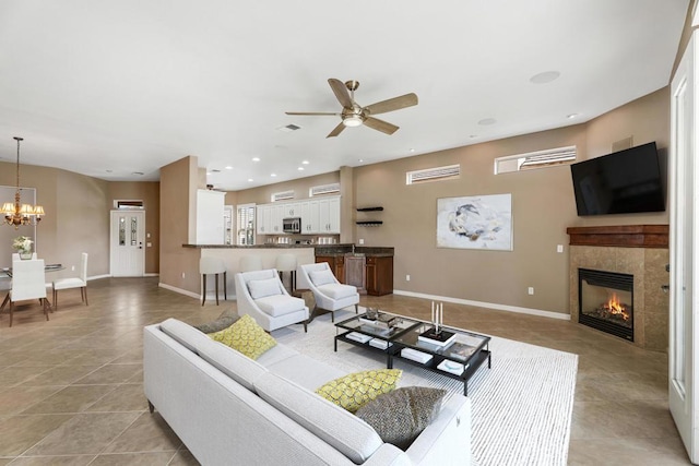 tiled living room featuring ceiling fan with notable chandelier and a tiled fireplace