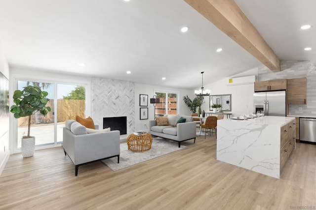 living room with vaulted ceiling with beams, a large fireplace, light hardwood / wood-style floors, and a notable chandelier