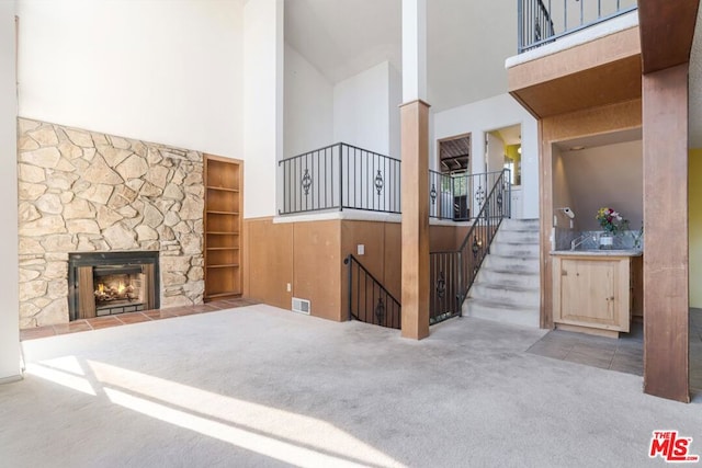 living room featuring carpet, built in features, a stone fireplace, and a towering ceiling