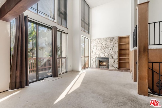 unfurnished living room featuring light carpet, a high ceiling, a stone fireplace, and beamed ceiling