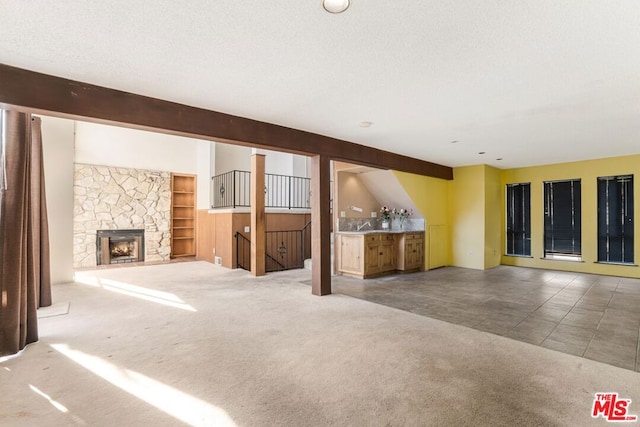 unfurnished living room with carpet, a textured ceiling, a stone fireplace, and beamed ceiling