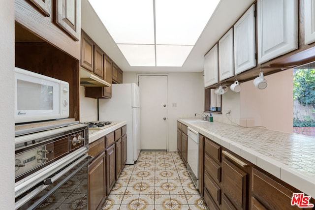 kitchen with kitchen peninsula, white appliances, sink, light tile patterned floors, and white cabinetry