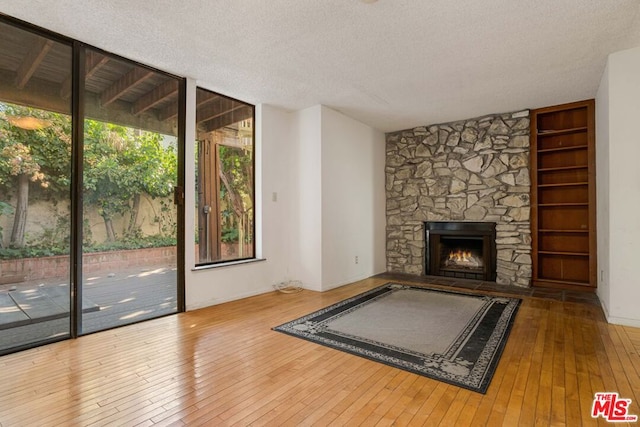 unfurnished living room with wood-type flooring, a textured ceiling, and a stone fireplace