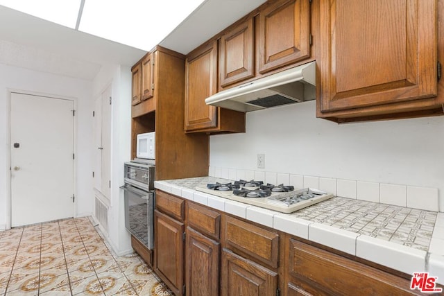 kitchen featuring tile counters, light tile patterned flooring, and white appliances