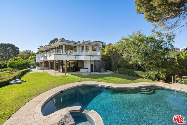 back of house featuring a yard, a swimming pool with hot tub, a balcony, and a patio